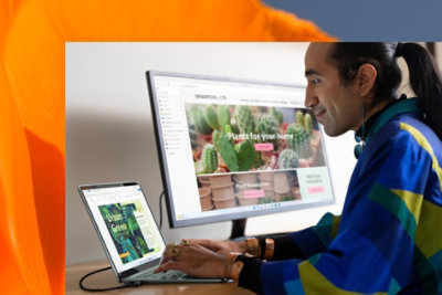 A person smiles while editing photographs on a Surface Laptop 5 using an external monitor.