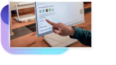 A hand reaching out to use a touchscreen monitor to send praise to colleagues.