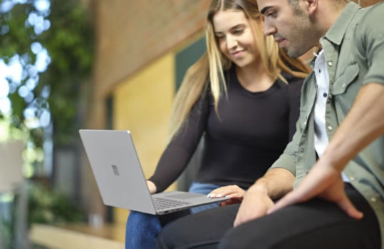 A woman looking at her phone with her Surface laptop in front of her.