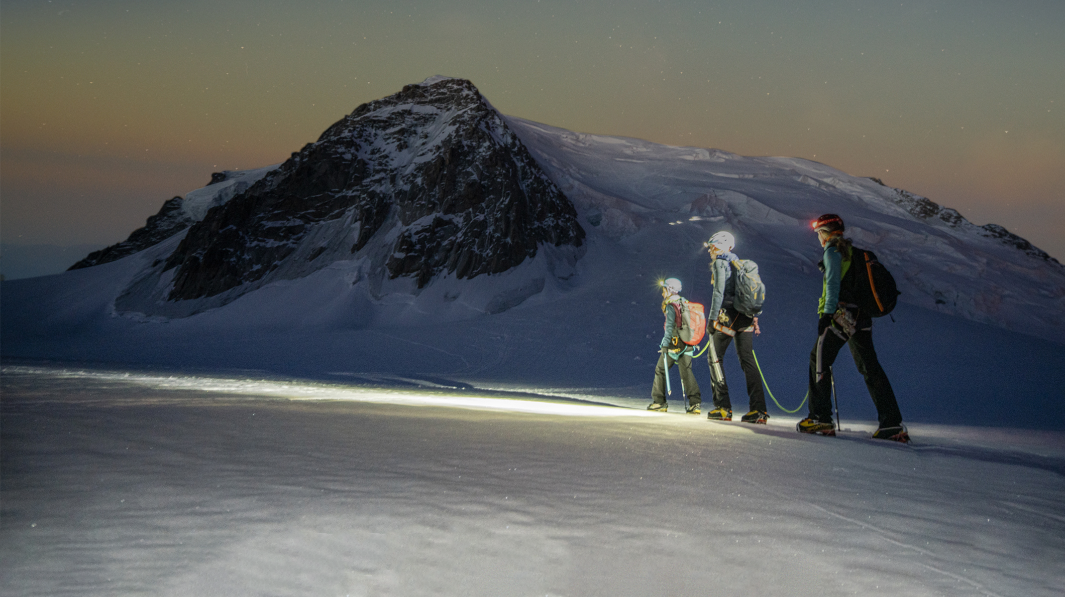 Three hikers traversing a snowy mountain under a starry sky