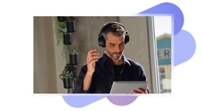 A person wearing over-the-ear headphones and holding a tablet.