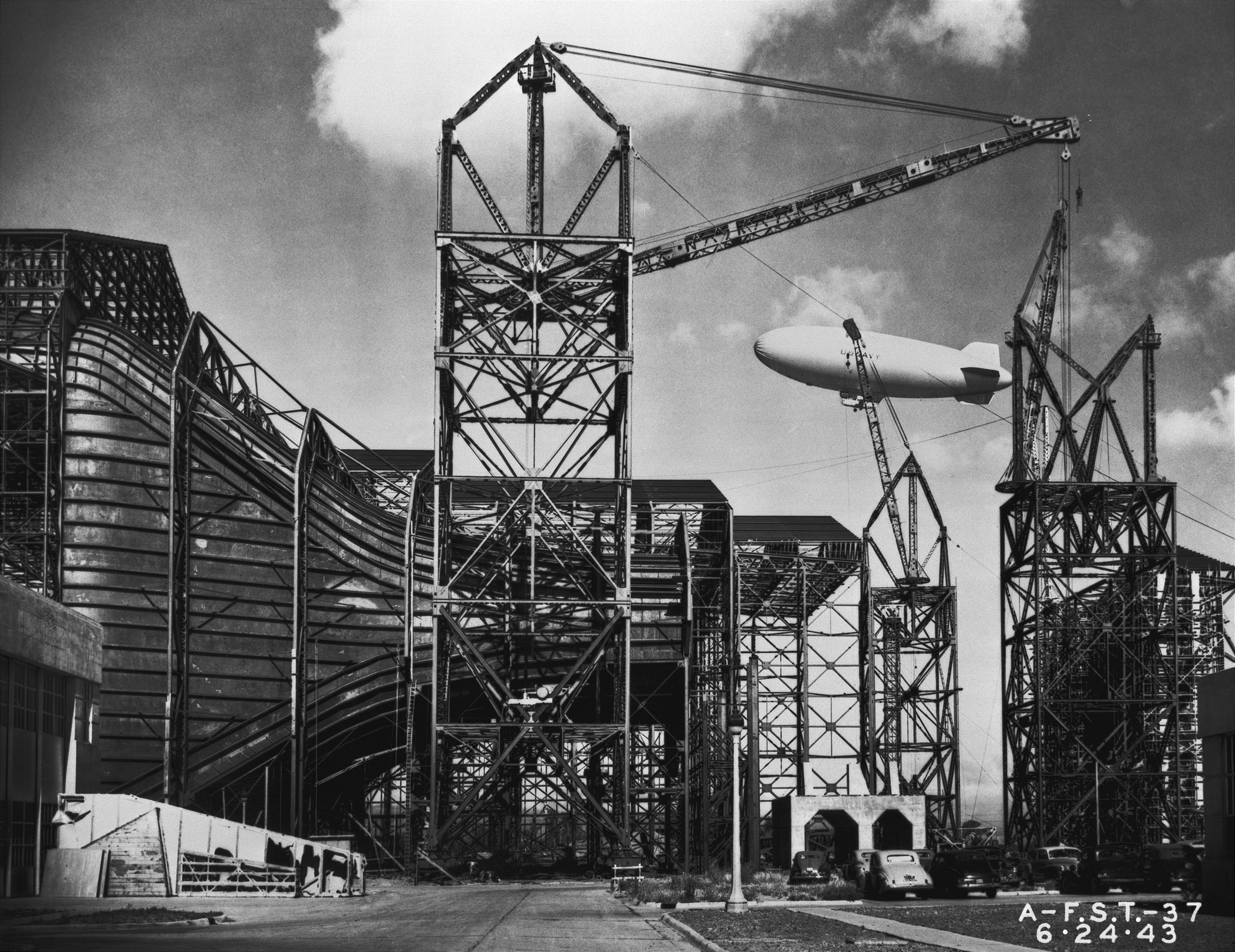 Construction of the Ames Full-Scale 440-by-80-foot wind tunnel. Side view of entrance cone, blimp in background.