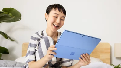 A person smiling while holding a sapphire Surface Pro 9 tablet