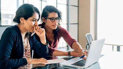 Zwei Personen, die an einem Schreibtisch sitzen und gemeinsam an einem Laptop arbeiten