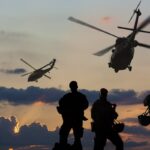 Three marines in the foreground with two helicopters in the background.