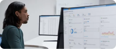 A man sitting in front of two monitors looking at data.