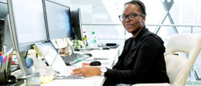 A woman sitting at a desk with two monitors.