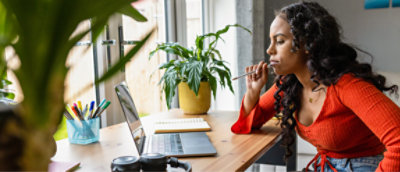 A woman sitting at a desk with a laptop and a plant in front of her.