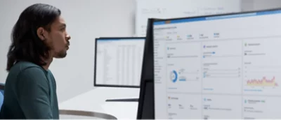 A man sitting in front of two monitors looking at data.