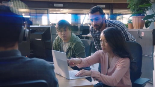 Shot of a woman pointing at the computer while her 2 coworkers look on.
