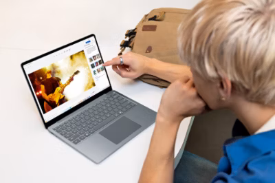 A person reviewing or editing a photo of a guitarist on a Surface laptop, with a backpack in the background